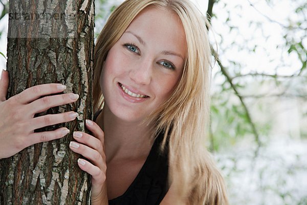 Portrait blond Frau umarmen lächeln Baum Baumstamm Stamm Haar