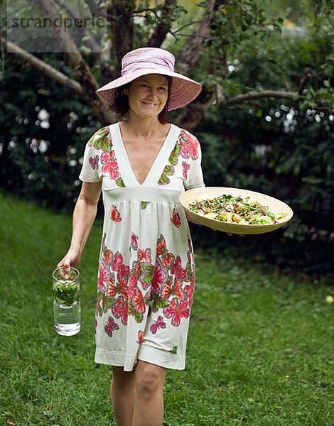 Frau in flowery Kleid mit Salat und Krug Wasser
