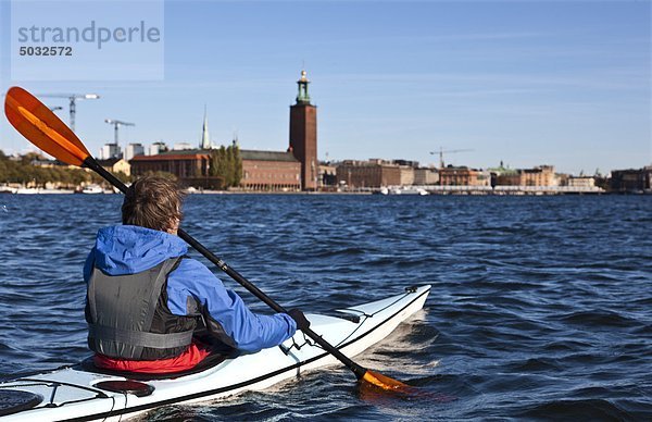 Man kayaking on sea  cityscape in background
