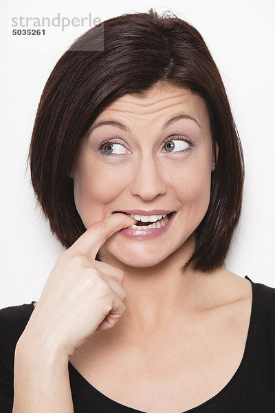 Nahaufnahme einer mittleren erwachsenen Frau mit Finger im Mund vor weißem Hintergrund  lächelnd