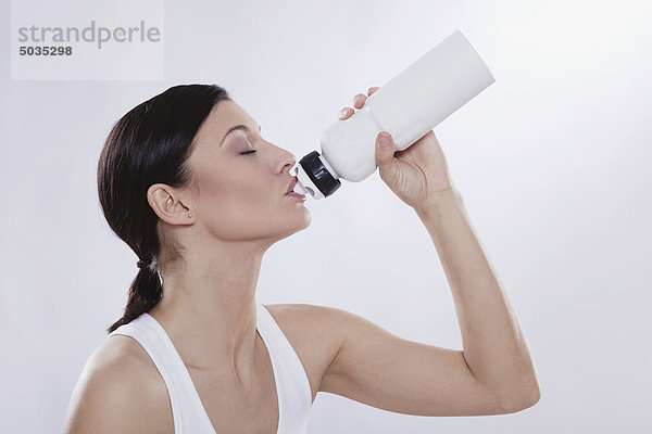 Mittlere erwachsene Frau trinkt aus der Wasserflasche vor weißem Hintergrund