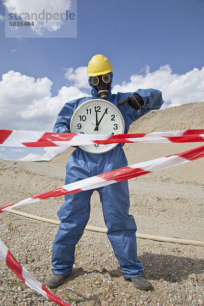 Mann in Schutzbekleidung mit Uhr bei Sanddüne und Kordonband im Vordergrund