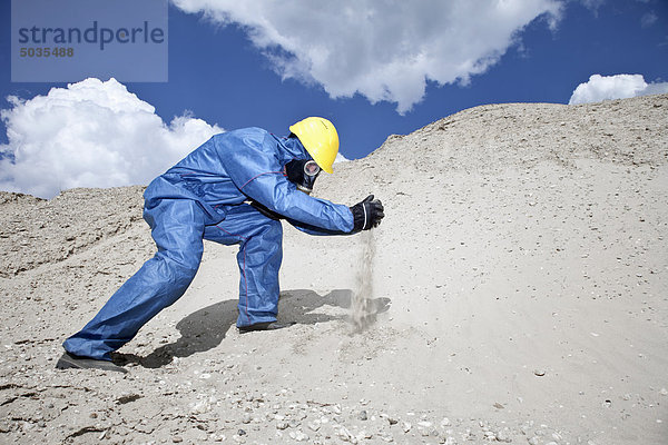 Mann in Schutzkleidung verschüttet Sand auf Sanddüne