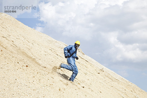 Mann in schützender Arbeitskleidung  der am Hang der Sanddüne läuft