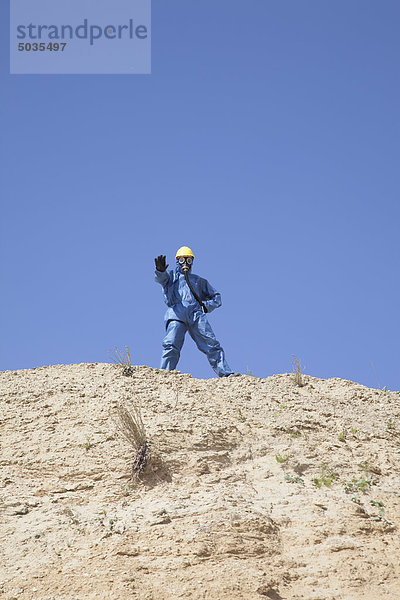 Mann in schützender Arbeitskleidung auf der Sanddüne stehend