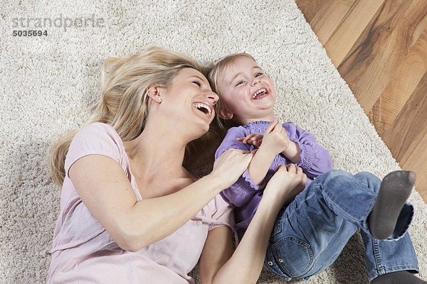 Deutschland  Bayern  München  Mutter und Tochter auf Teppich liegend  lachend