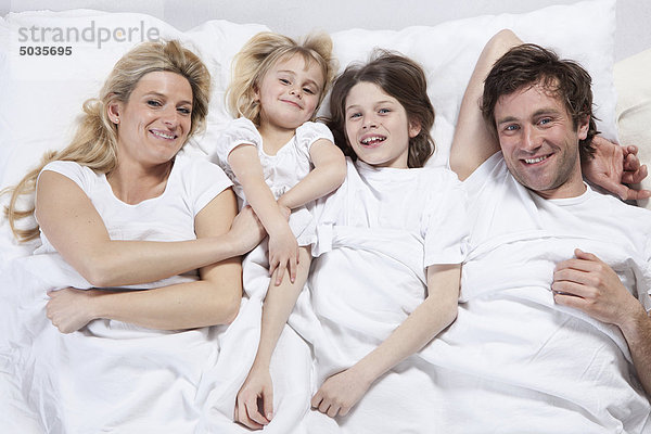 Deutschland  Bayern  München  Familie im Bett liegend  lächelnd  Portrait