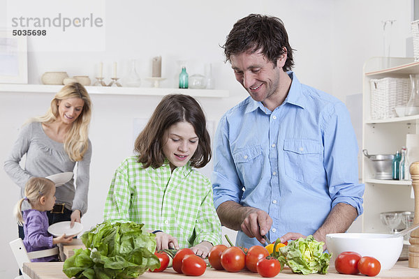 Deutschland  Bayern  München  Sohn bereitet Salat mit Vater  Mutter und Tochter im Hintergrund zu.