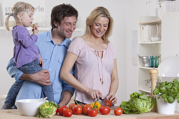 Deutschland  Bayern  München  Mutter bereitet Salat zu  Vater und Tochter stehen neben ihr.