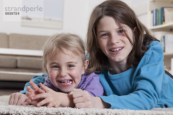 Junge und Mädchen auf Teppich liegend  lächelnd  Portrait