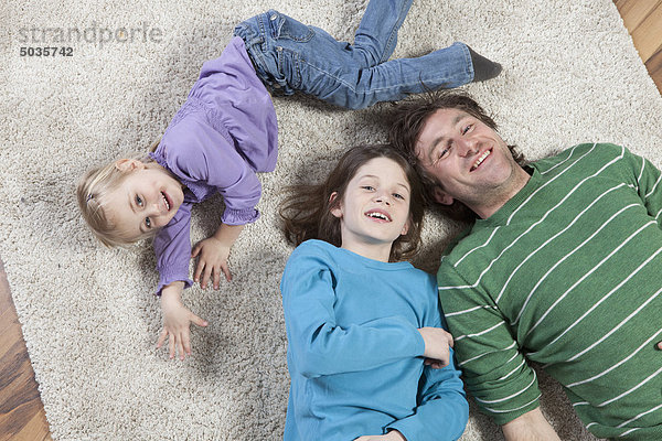 Deutschland  Bayern  München  Vater auf Teppich liegend mit Sohn und Tochter