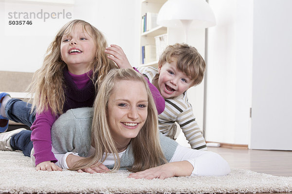 Deutschland  Bayern  München  Mutter  Tochter und Sohn liegen zu Hause auf dem Boden.