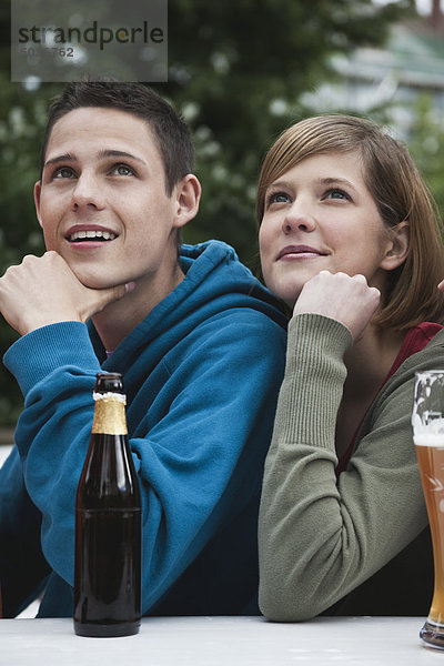 Junger Mann und Frau  die mit der Hand auf dem Kinn wegblicken.