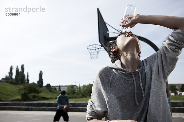 Teenager-Junge  der Wasser ins Gesicht gießt  während der Junge im Hintergrund spielt.