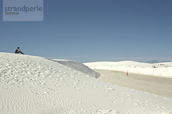 Frau sitzt auf einer Sanddüne mit Blick auf die Straße in White Sands National Monument  New Mexico  USA