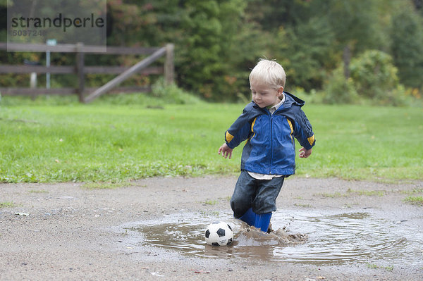 Little Junge spielt mit seiner Fußball in einer Pfütze  Ontario  Kanada