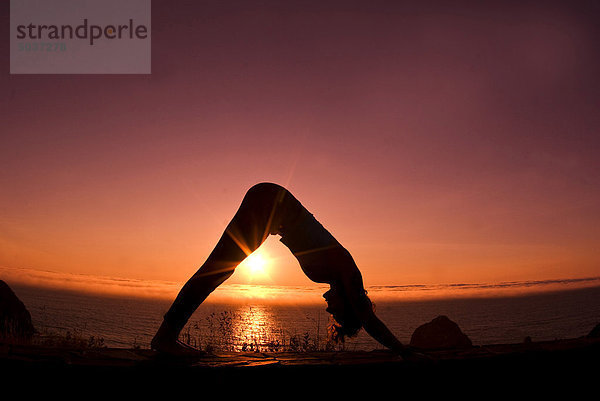 21 Jahre alte Frau in nach unten Hund Yoga Position an Meeresküste bei Sonnenuntergang