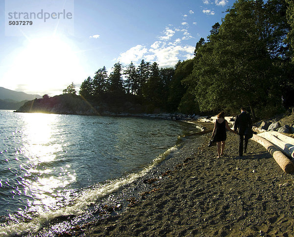 Gut gekleideter Mann und Frau zu Fuß auf felsigen Strand hält hände auf spät Sommernachmittag