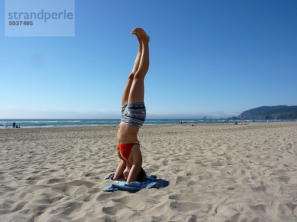Junge Frau im Yoga Kopfstand an sonnigen Tag in Cannon Beach  Oregon  USA