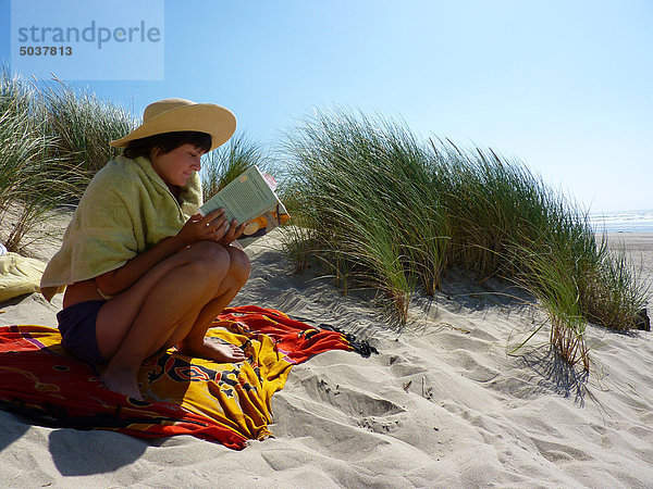 Junge Frau sitzend Lesung Buch über Sanddüne in Cannon Beach  Oregon  USA