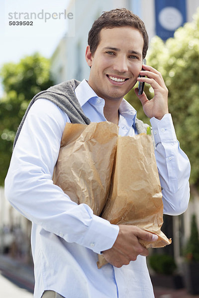 Mittlerer Erwachsener Mann spricht auf einem Handy mit Papiertüten voller Gemüse