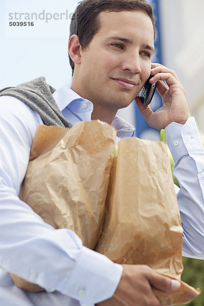 Mittlerer Erwachsener Mann spricht auf einem Handy mit Papiertüten voller Gemüse