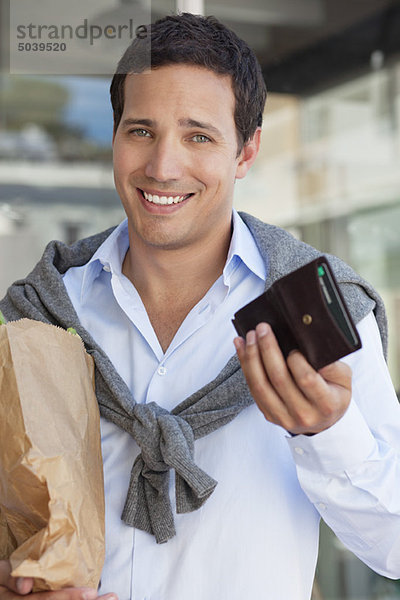 Porträt eines Mannes mit leerer Brieftasche und Papiertüte voller Gemüse