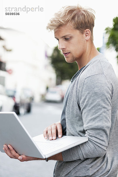 Junger Mann mit einem Laptop auf der Straße