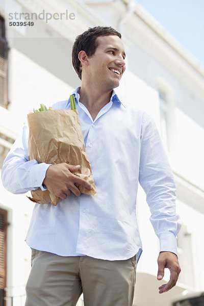 Ein erwachsener Mann hält eine Papiertüte voller Gemüse und lächelt.