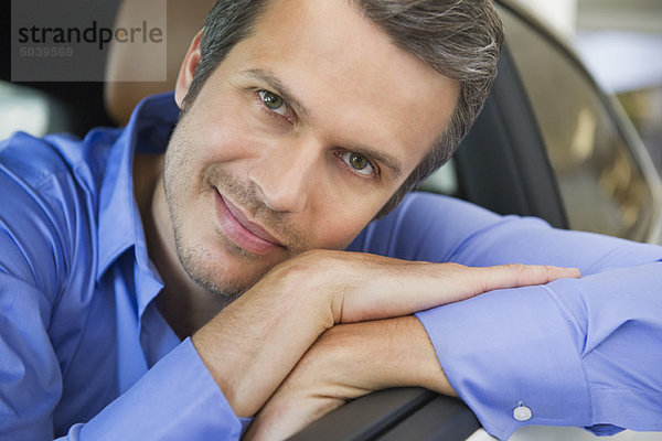 Porträt eines fröhlichen  erwachsenen Mannes  der sich an die Autoscheibe lehnt.