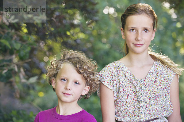 Porträt von süßen kleinen Geschwistern  die zusammen in einem Garten spazieren gehen.