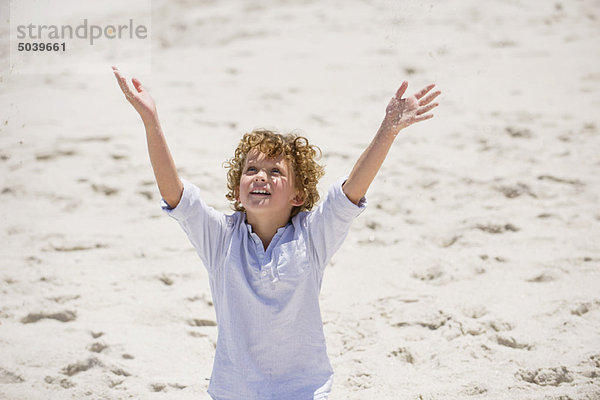 Junge steht mit erhobenen Armen am Strand.