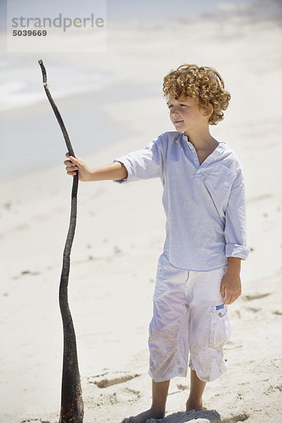 Junge mit Holzstab am Strand