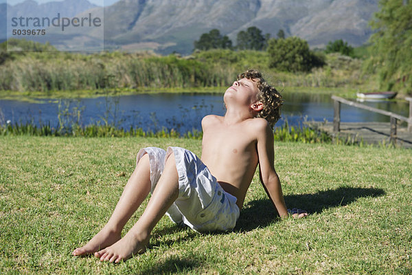 Hemdenloser kleiner Junge sitzt mit geschlossenen Augen gegen den Berg.