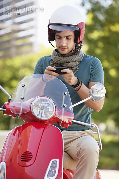 Mann sitzt auf einem Roller und SMS