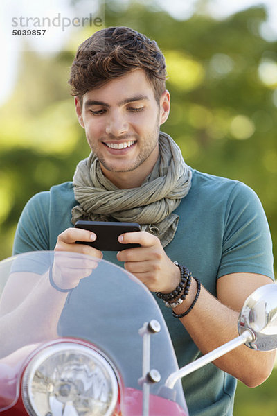 Mann sitzt auf einem Roller und SMS