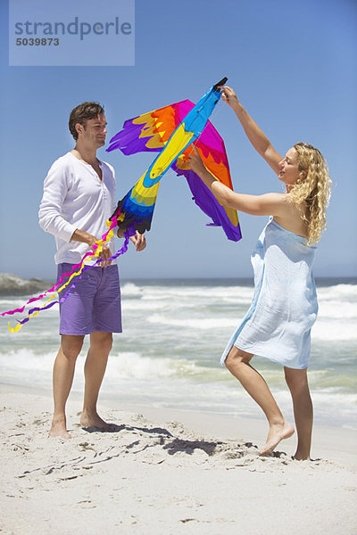 Mittleres erwachsenes Paar  das einen Drachen in Tierform am Strand hält.