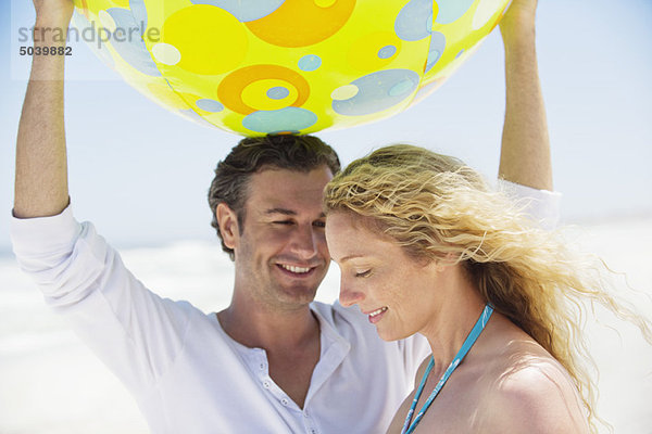 Mann hebt einen Strandball und lächelt mit einer Frau in seiner Nähe