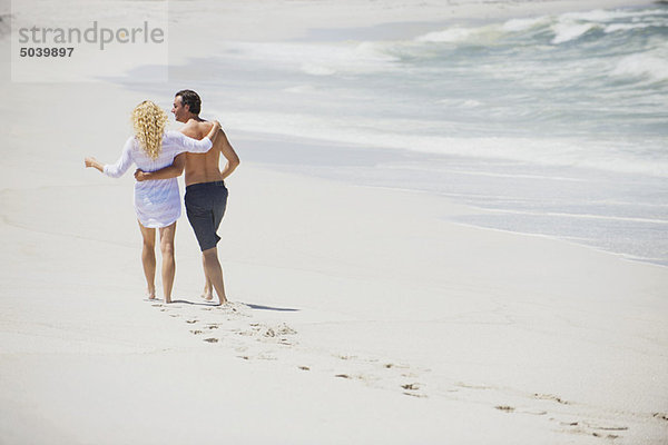 Rückansicht eines Paares  das mit den Armen um den Strand läuft