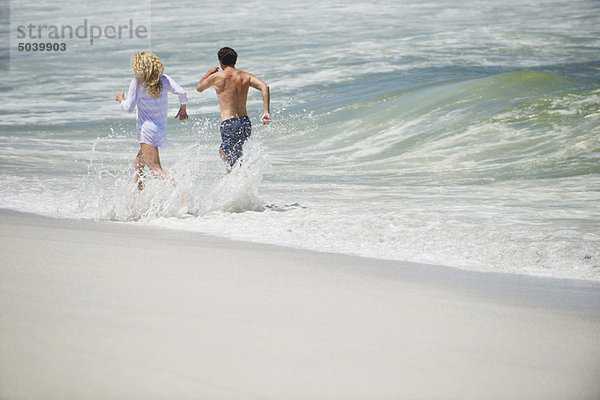 Rückansicht eines am Strand laufenden Paares