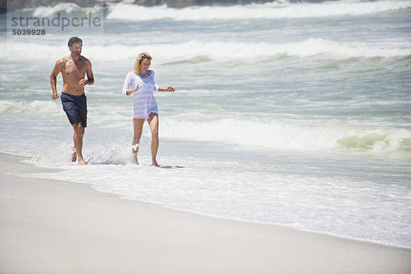 Mittleres erwachsenes Paar  das am Strand läuft