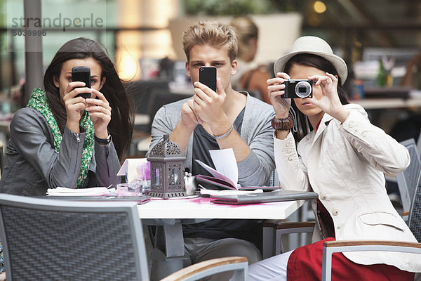 Drei junge Freunde mit elektronischen Gadgets in einem Restaurant