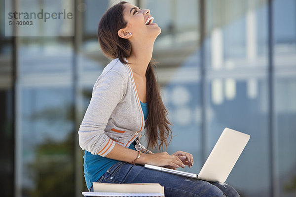 Frau lacht bei der Benutzung eines Laptops