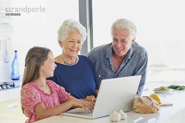 Mädchen  das einen Laptop benutzt  während ihre Großeltern sie in der Küche anschauen.