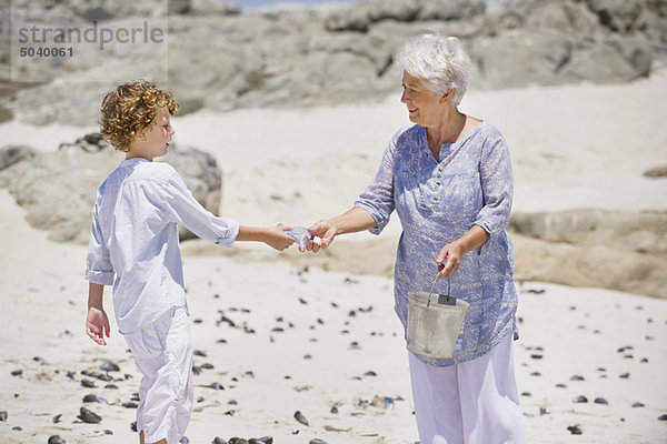 Seniorin mit ihrem Enkel beim Muschelsammeln am Strand