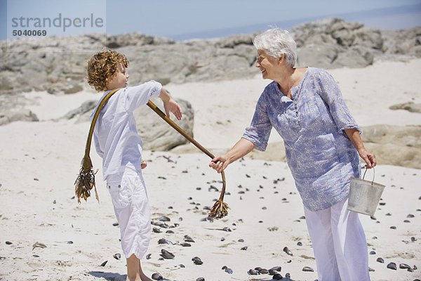 Seniorin mit ihrem Enkel beim Muschelsammeln am Strand
