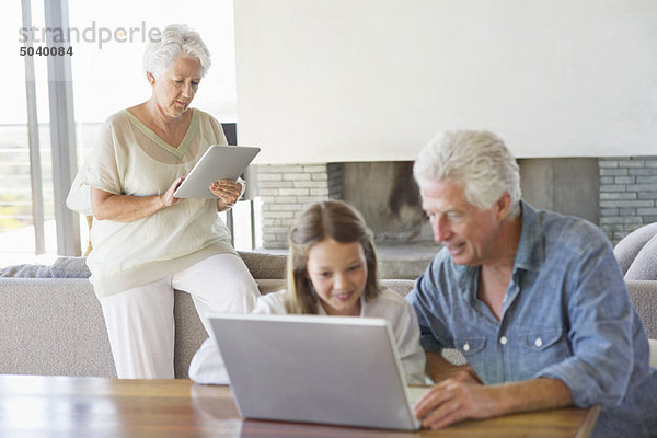 Mann  der mit seiner Enkelin und seiner Frau einen Laptop benutzt und im Hintergrund an einem digitalen Tablett arbeitet.