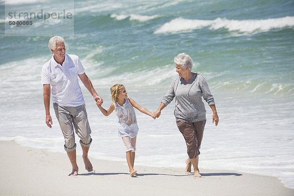 Seniorenpaar  das mit seiner Enkelin am Strand spazieren geht.