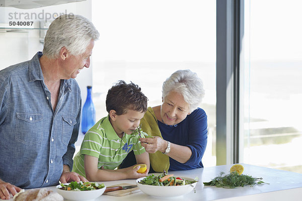 Junge  der Gemüse riecht  während seine Großeltern neben ihm in der Küche stehen.