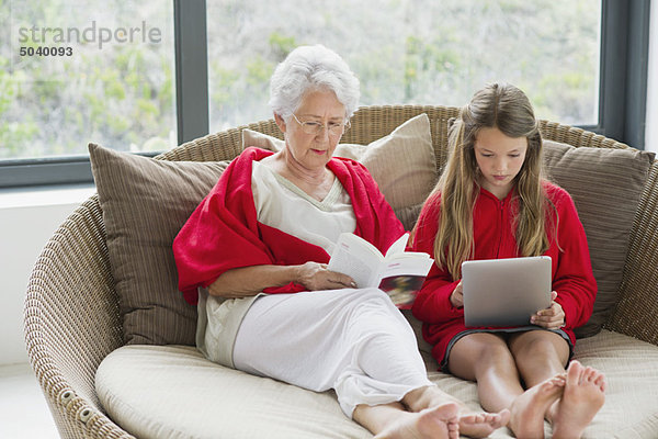 Seniorin beim Lesen einer Zeitschrift mit ihrer Enkelin auf einem digitalen Tablett